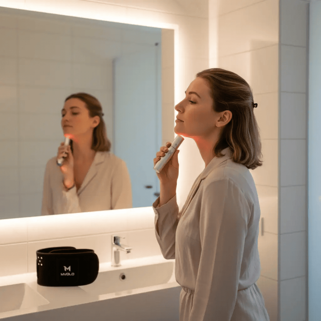 Vrouw gebruikt roodlichttherapie-apparaat op kaaklijn als onderdeel van haar acne-routine thuis