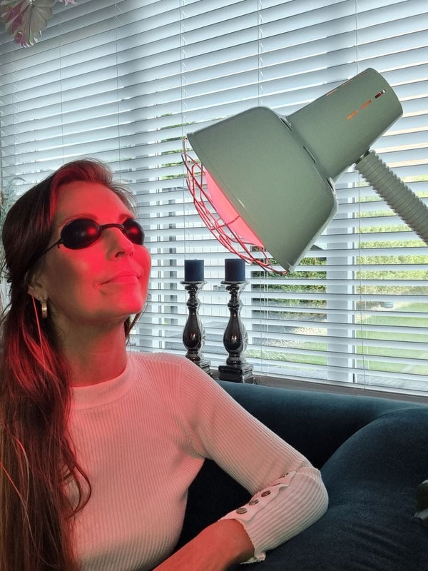 Vrouw gebruikt roodlichttherapie lamp met beschermbril voor gezichtsverzorging binnenshuis