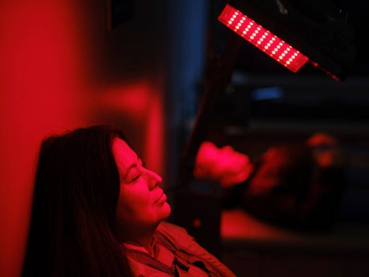 Persoon die ontspant onder een roodlichttherapie lamp in een donkere ruimte.